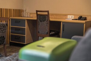 Habitación pequeña con un escritorio de madera, una silla, un mueble bajo y un objeto verde en primer plano.