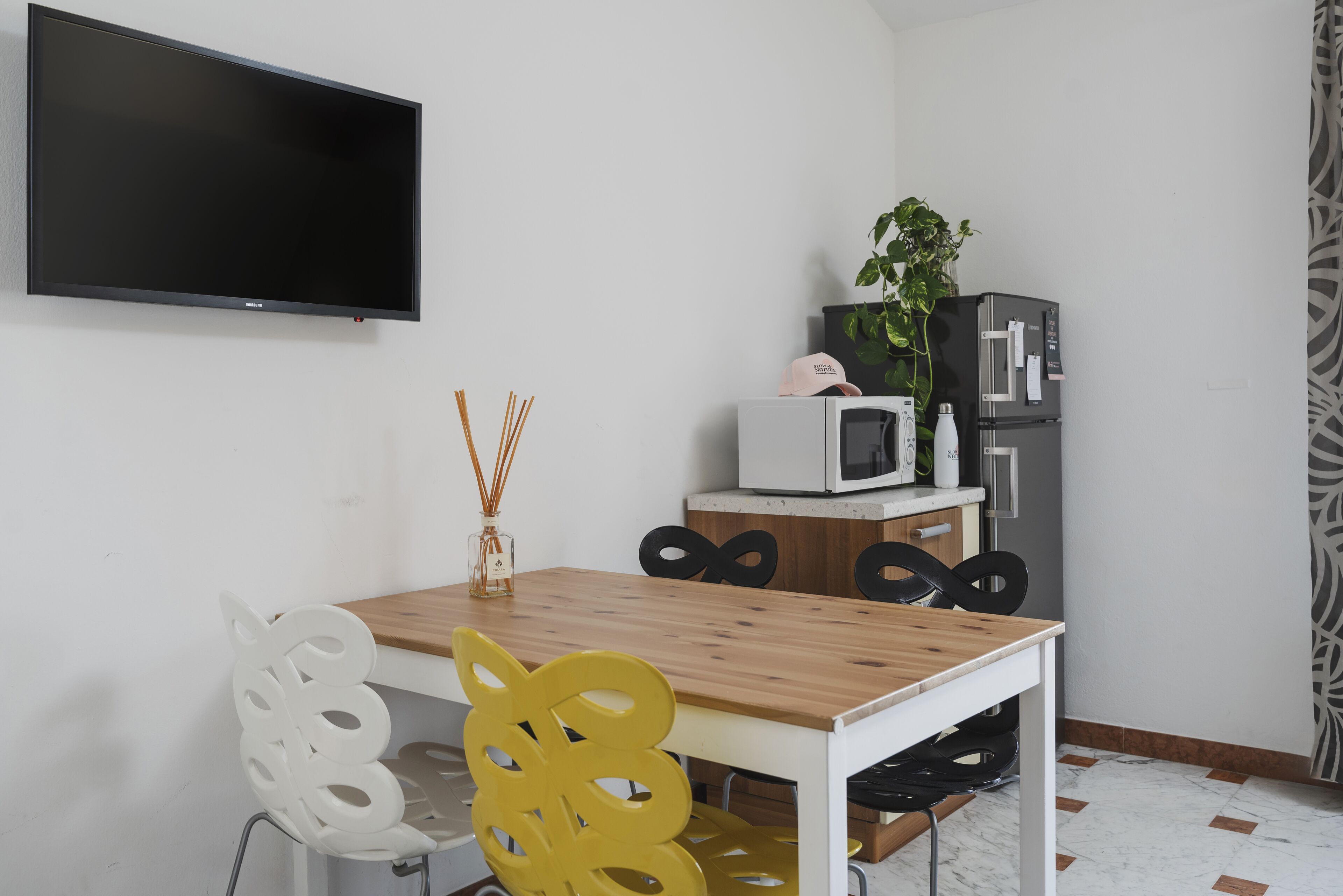 A modern kitchen with a wooden table, white chairs, a flat-screen TV, a microwave, and a refrigerator.
