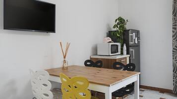 Una cucina moderna con tavolo in legno, sedie bianche, TV a schermo piatto, forno a microonde e frigorifero.