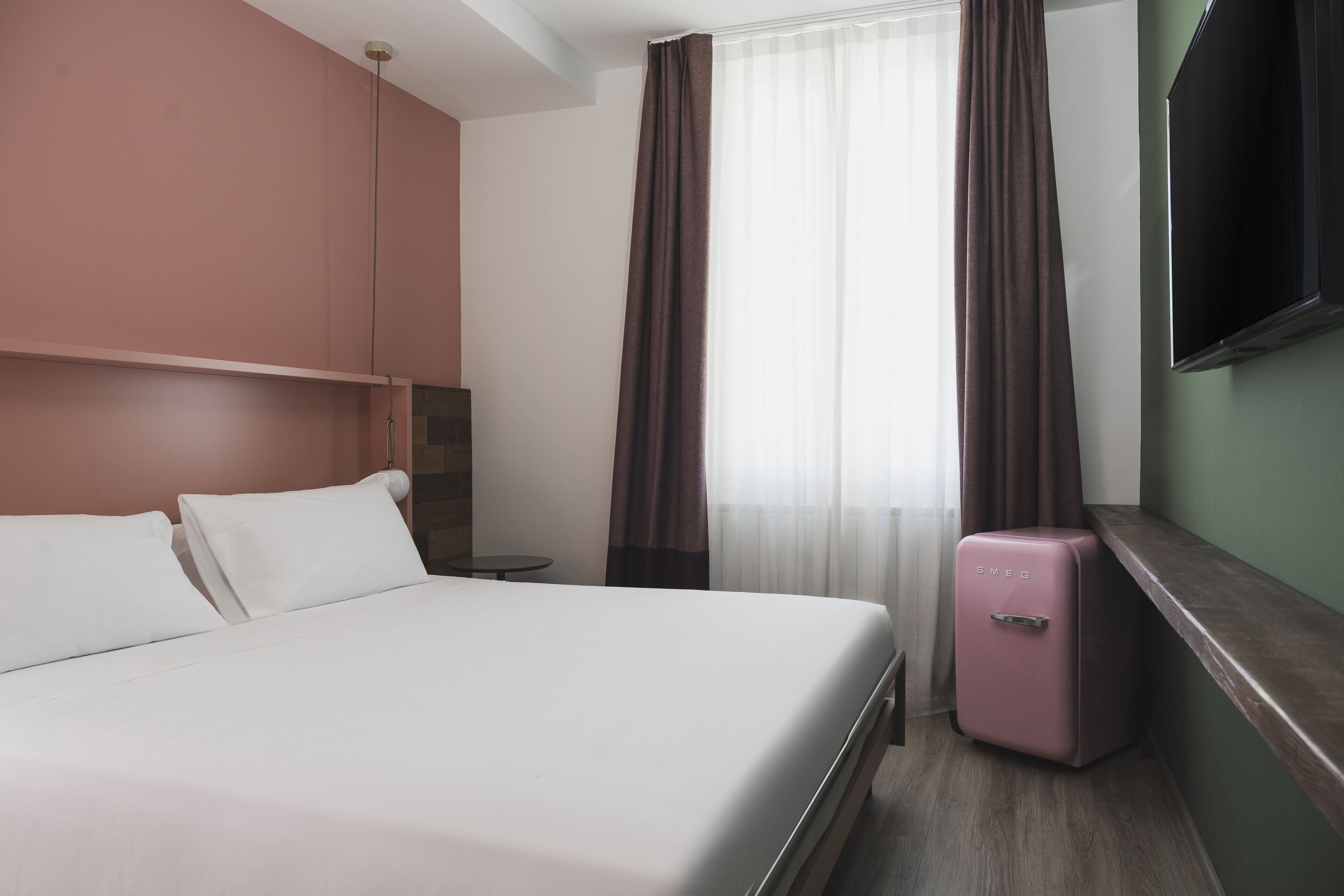 A hotel room with a bed, a small table, a TV, and a minibar.