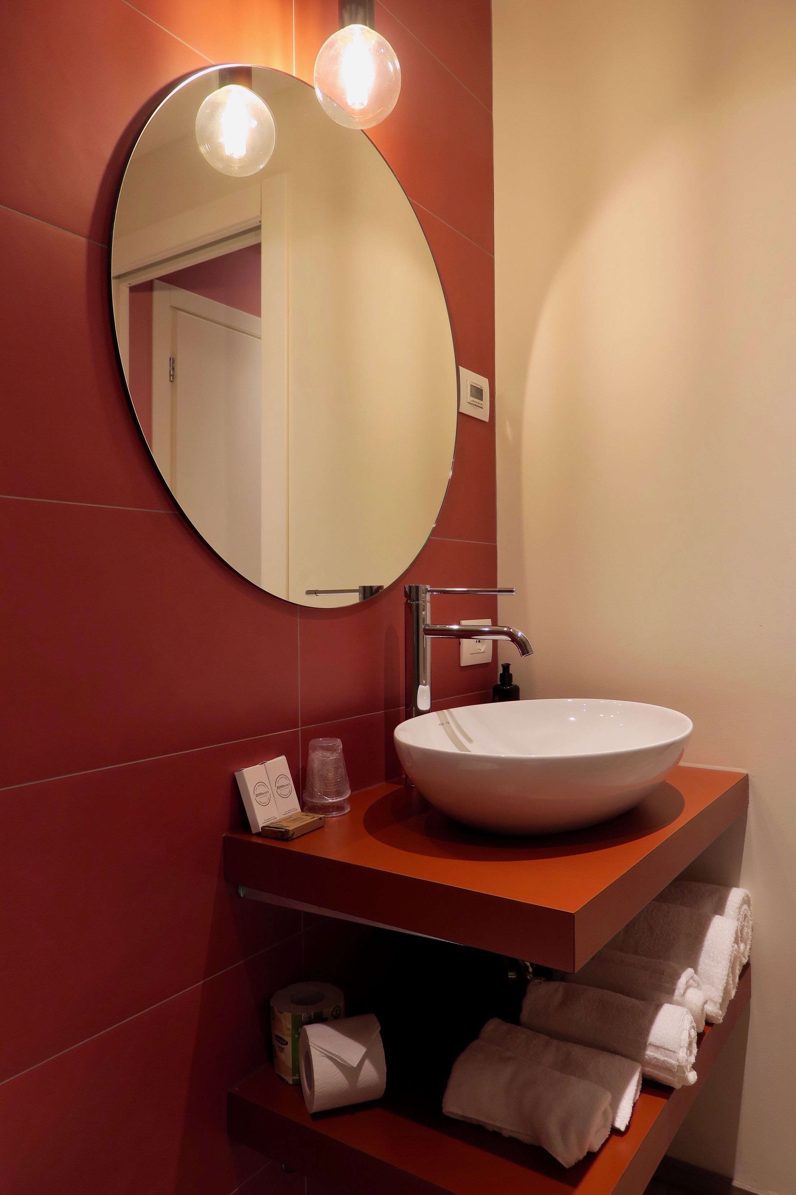 A modern bathroom with a round mirror, a white sink, and a towel rack.
