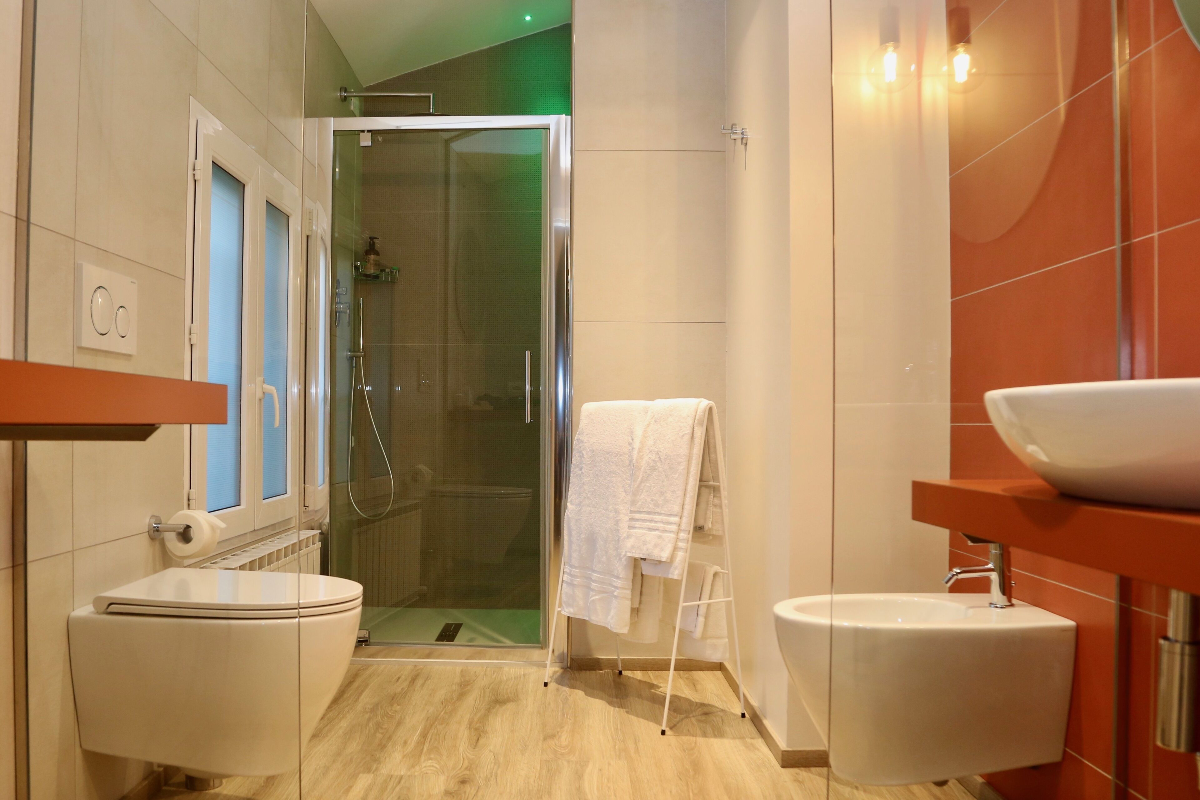 A modern bathroom with a glass shower enclosure, a white toilet, and a sink with a red countertop.