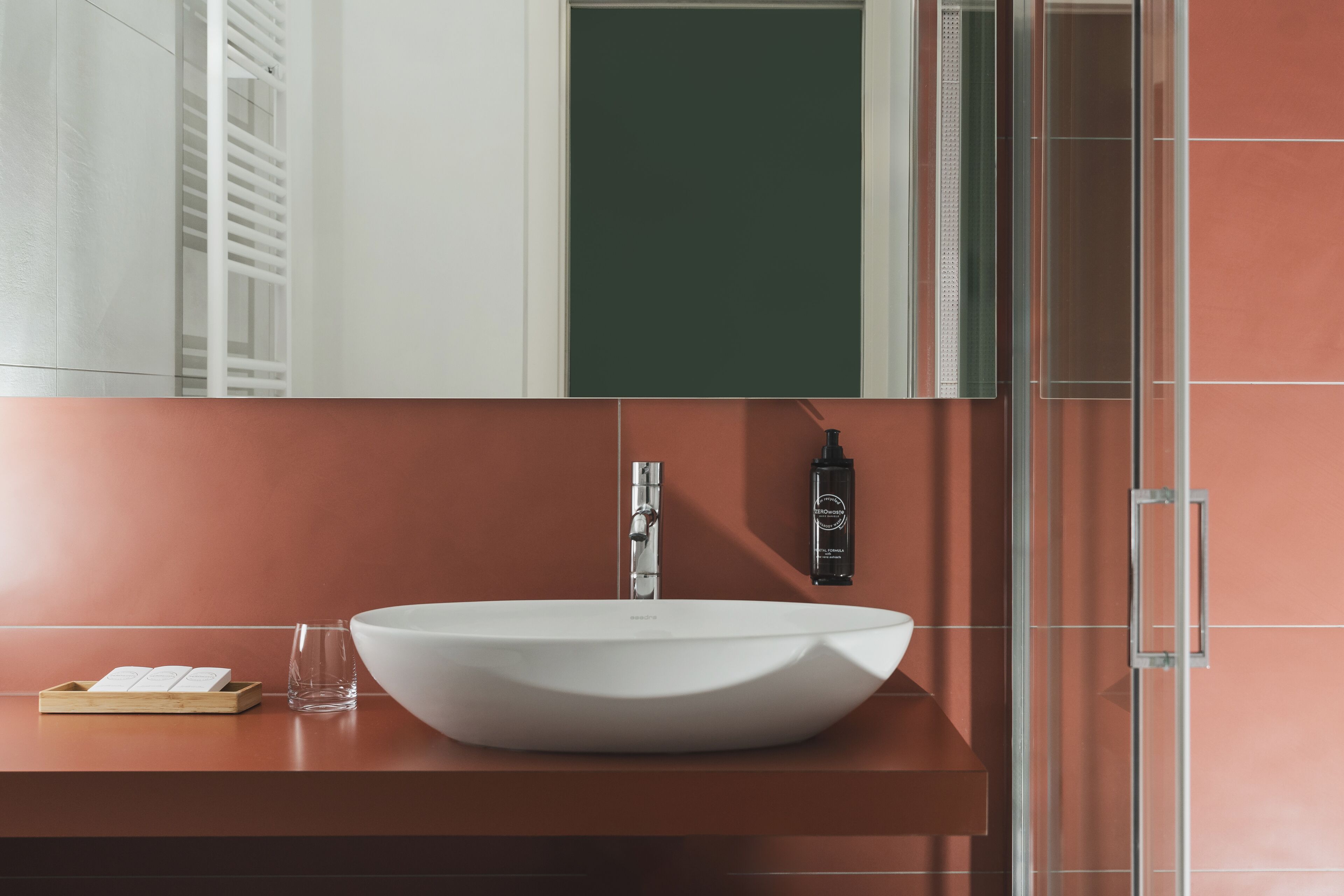Ein modernes Badezimmer mit einem weißen Waschtischbecken, einem Glas und einer kleinen Holztablett.