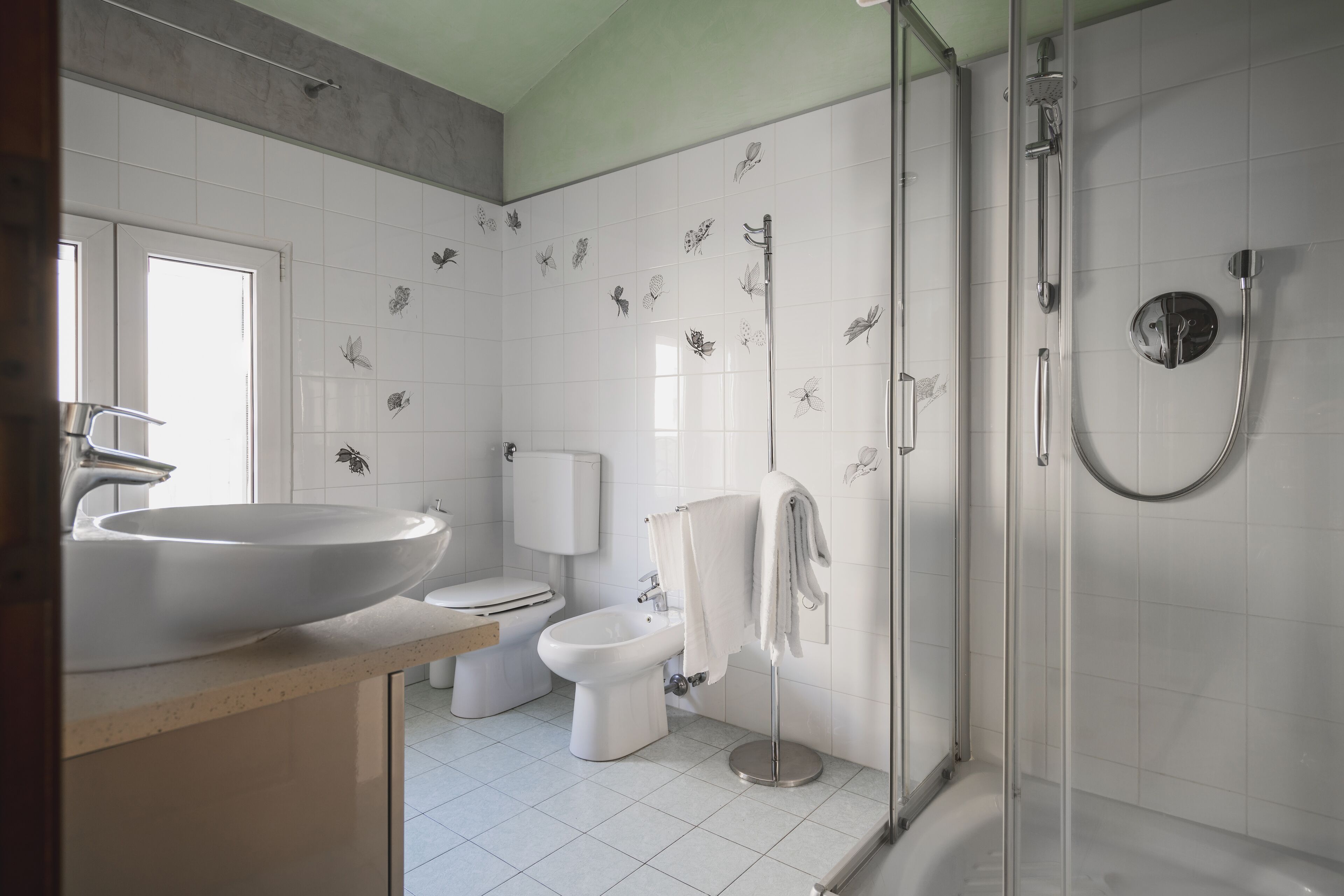 A modern bathroom with a large sink, toilet, bidet, and a walk-in shower.