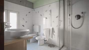 A modern bathroom with a large sink, toilet, bidet, and a walk-in shower.