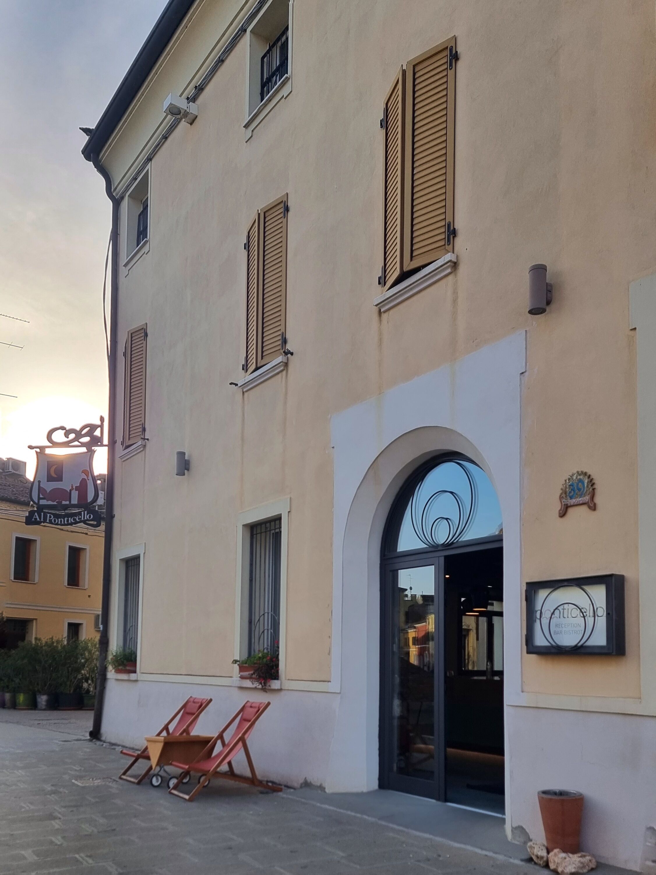 A building with a large arched entrance, multiple windows with shutters, and outdoor seating.