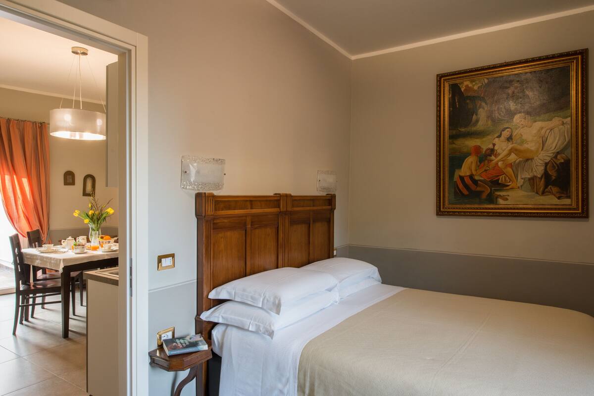 Une chambre d’hôtel avec une tête de lit en bois, un tableau au mur et un coin repas comprenant une table et des chaises.