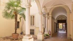 Un pasillo con arcos, columnas y una palmera en maceta.