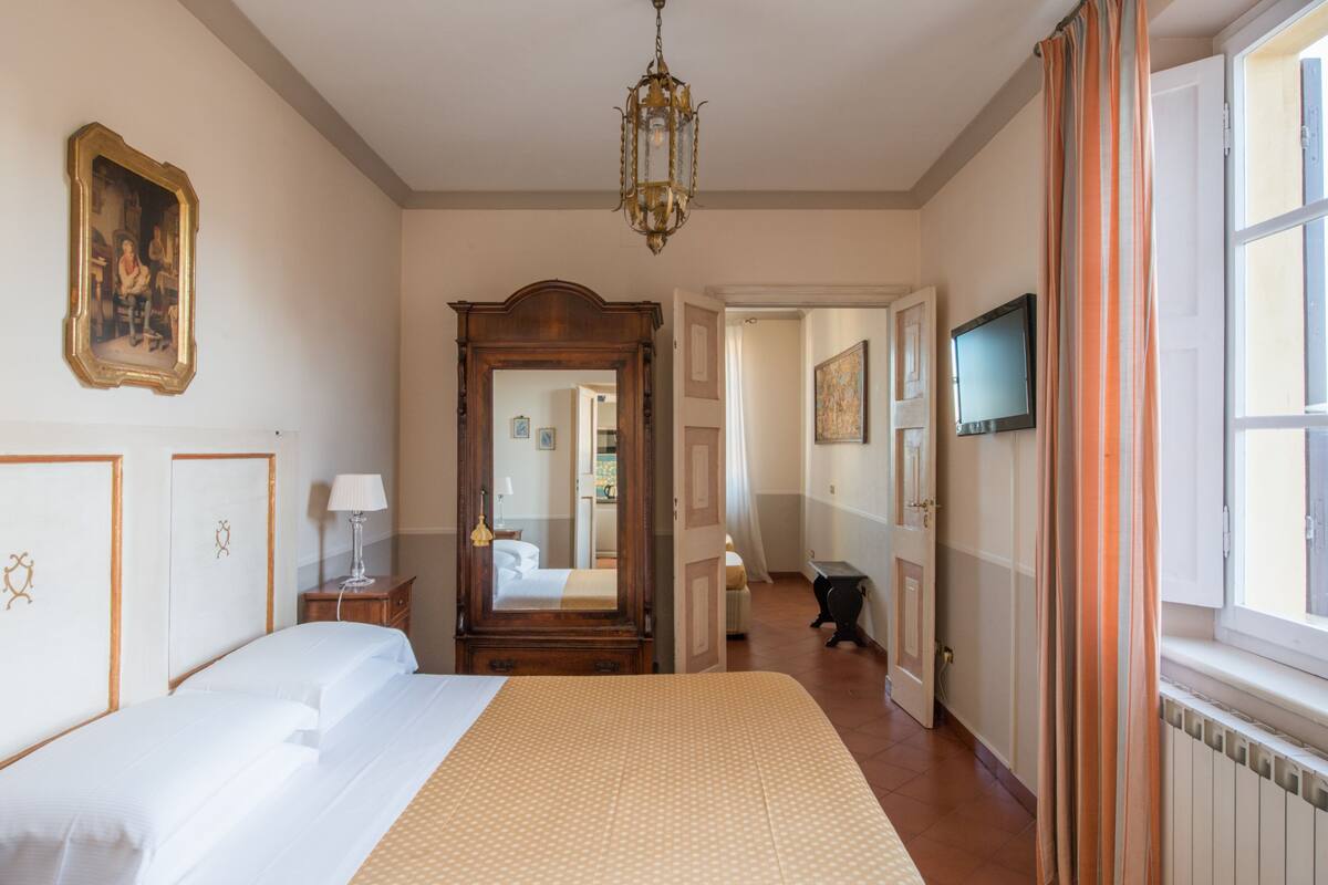 Une chambre d’hôtel avec un grand lit, un miroir, une télévision et une fenêtre avec des rideaux.