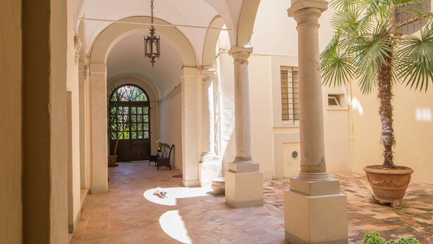 Un pasillo con arcos, columnas y una palmera.