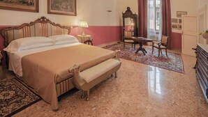 Habitación de hotel con una cama grande, un banco, un escritorio, una silla, un espejo y un aparador.