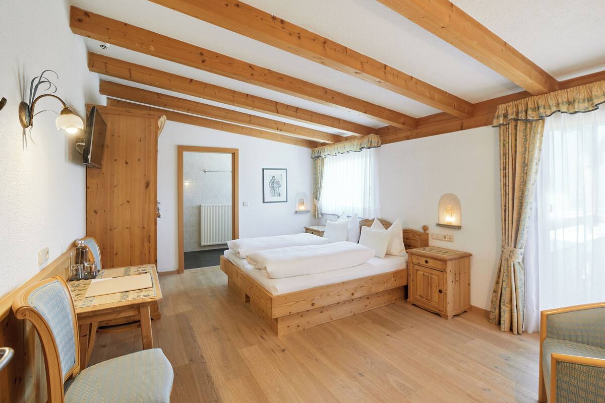 Un dormitorio de madera con cama, mesitas de noche, escritorio y una silla.