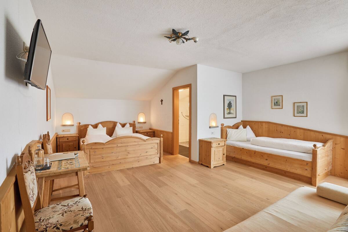 Una habitación con muebles de madera, una cama, un sofá, un escritorio y un televisor montado en la pared.