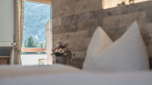 Een slaapkamer met een bed, een houten hoofdbord en uitzicht op een bergachtig landschap door een raam.