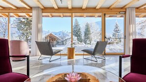 Een modern interieur met een houten plafond, grote ramen en twee stoelen met uitzicht op een besneeuwde berg.