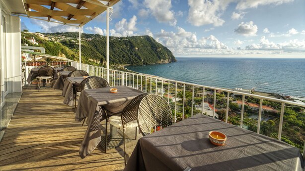A terrace with tables and chairs overlooking a coastal view. - Panoramahotel by Imperamare (Forio)