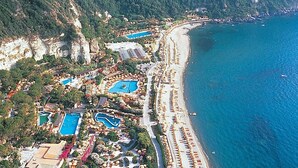An aerial view of a coastal resort with multiple swimming pools, a long beachfront, and lush greenery. - Panoramahotel by Imperamare (Forio)
