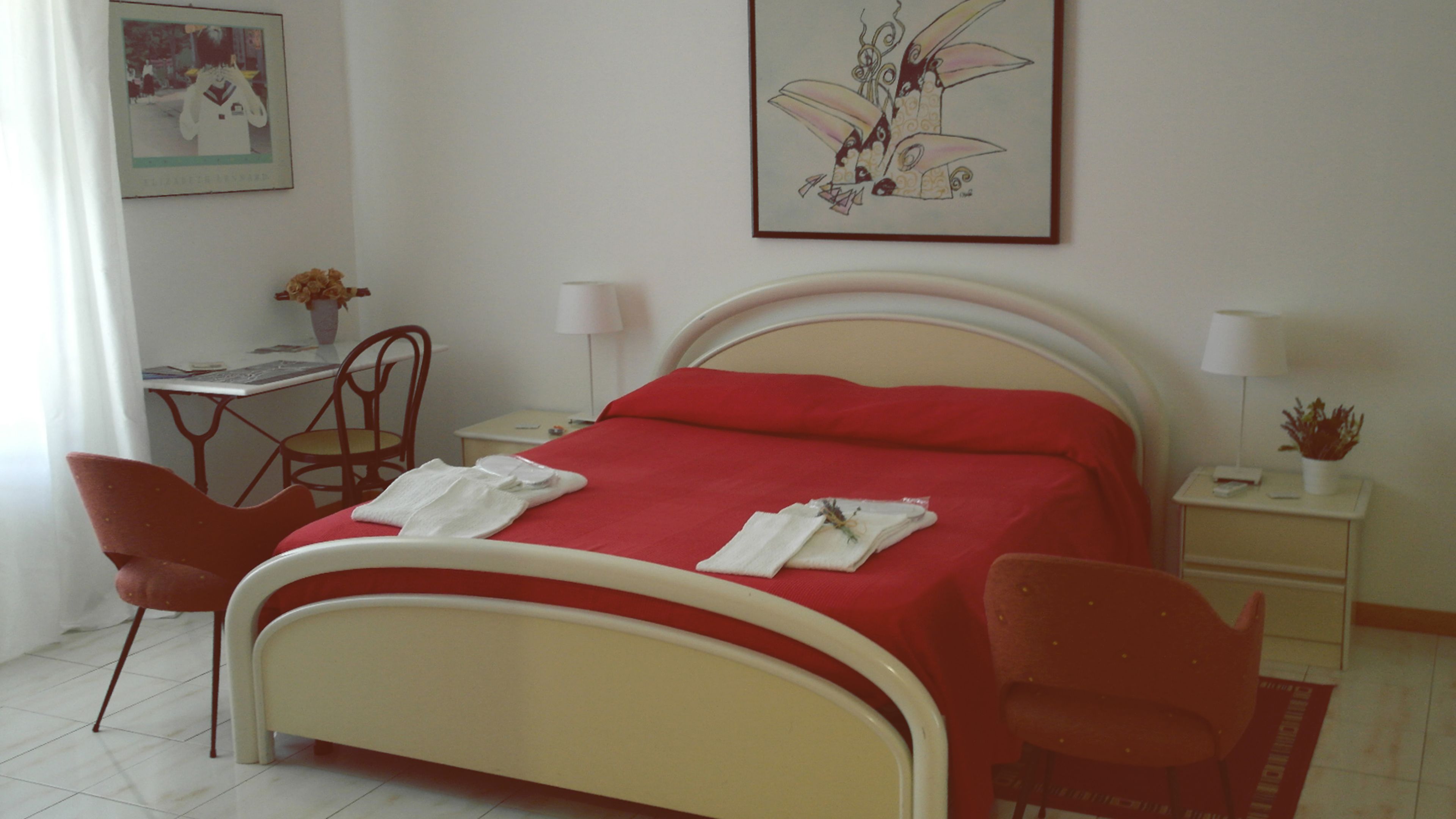 A hotel room with a bed, two chairs, a desk, a lamp, and a framed picture on the wall.