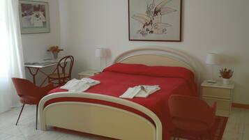 A hotel room with a bed, two chairs, a desk, a lamp, and a framed picture on the wall.