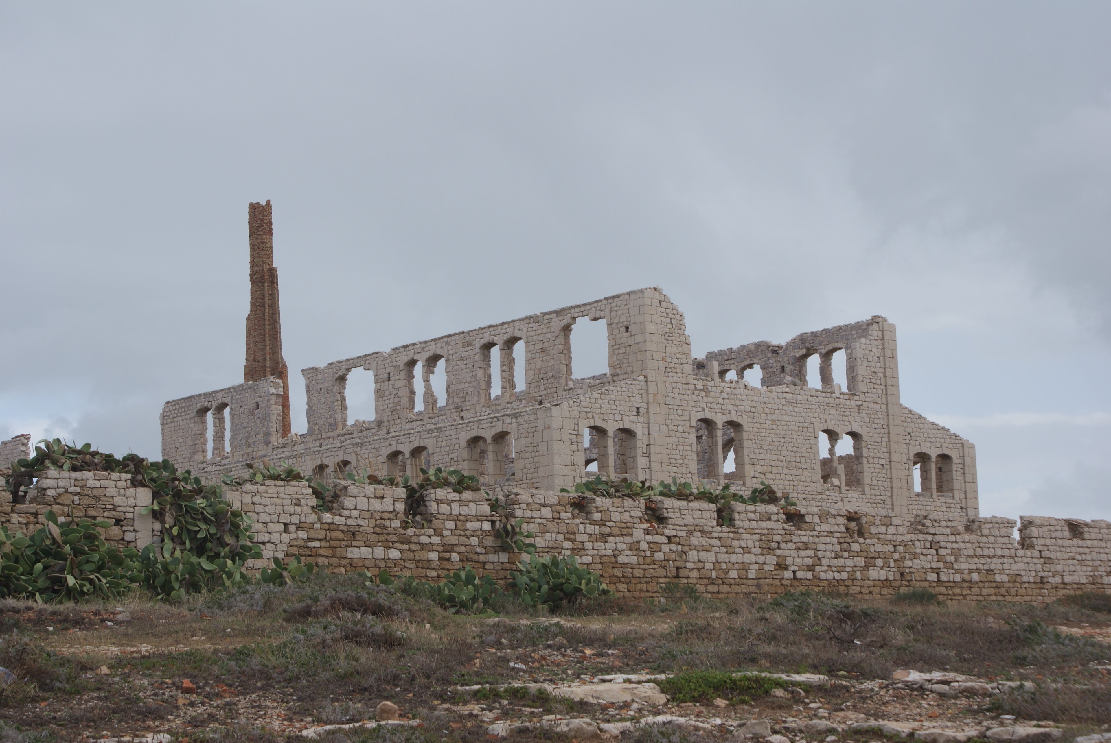 A large, abandoned building with multiple arches and a tall chimney.