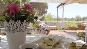 Un patio con una mesa dispuesta para una comida, una planta en maceta y una persona al fondo.