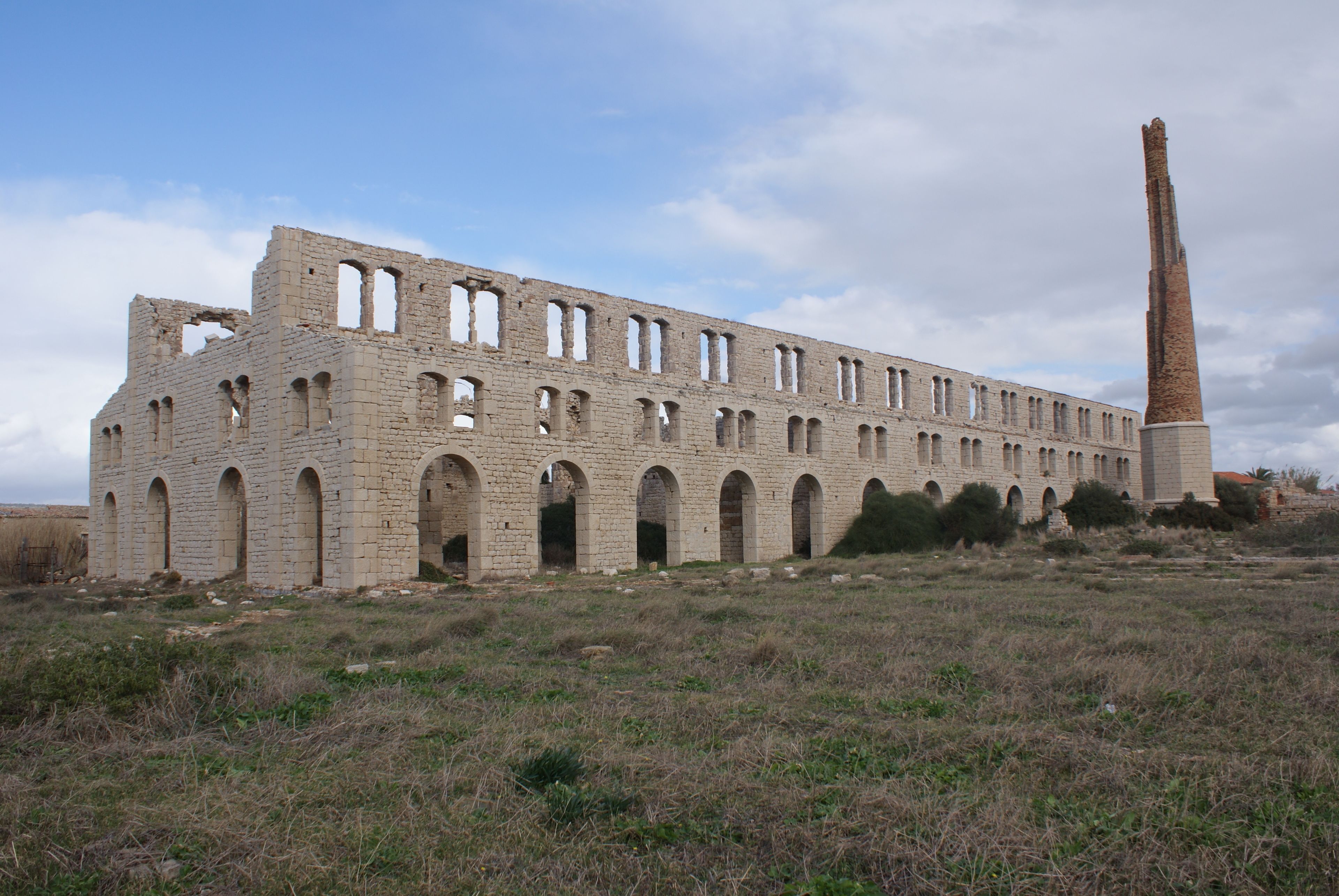 Um edifício grande e histórico com várias arcos e uma chaminé alta.