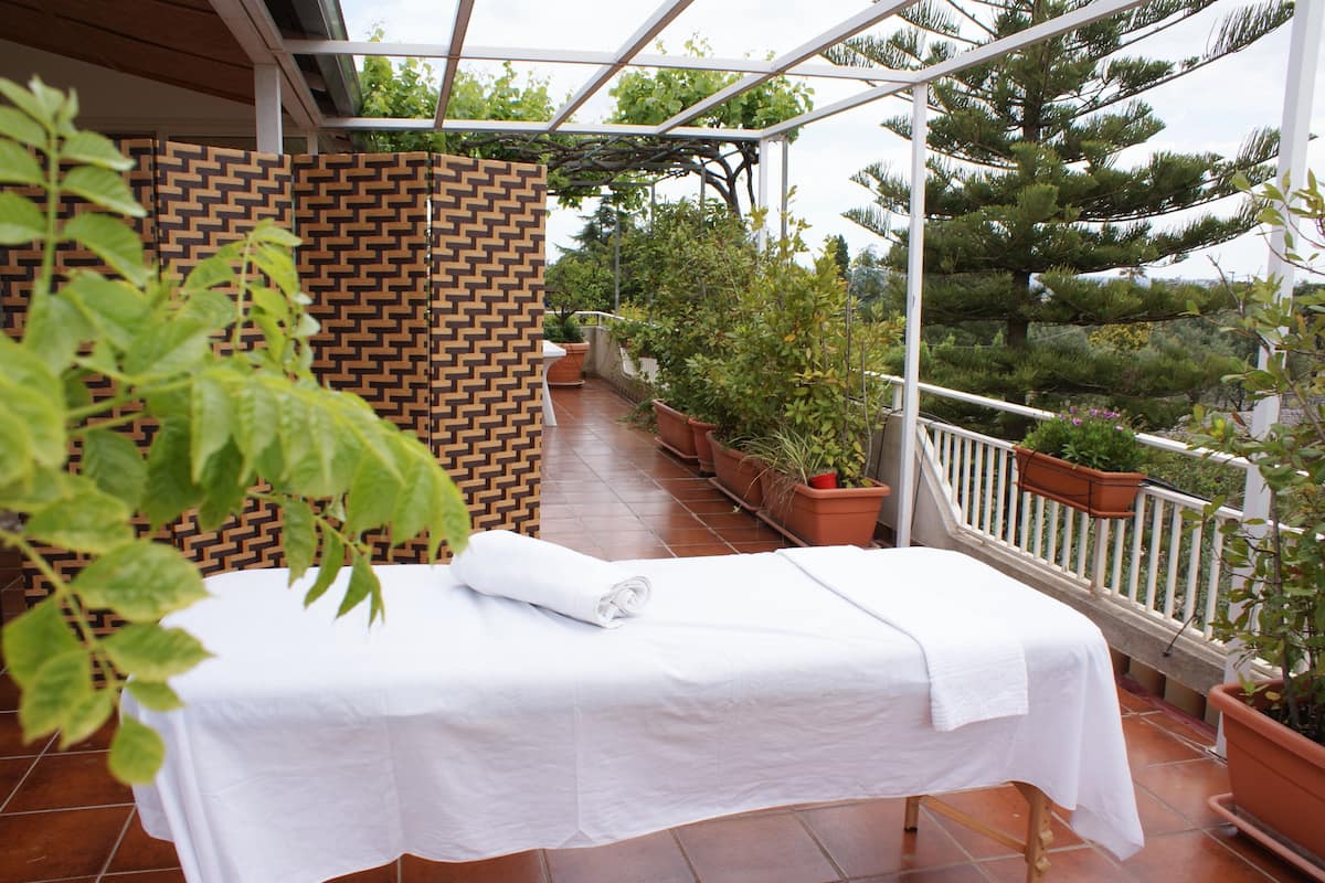 A massage table with a white sheet, surrounded by potted plants and a brick wall on a balcony.