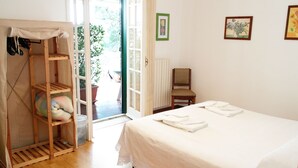 A bedroom with a bed, a chair, a wooden shelf with a cushion, and a door leading to an outdoor area. - Giogaia Bed & Breakfast (Modica)