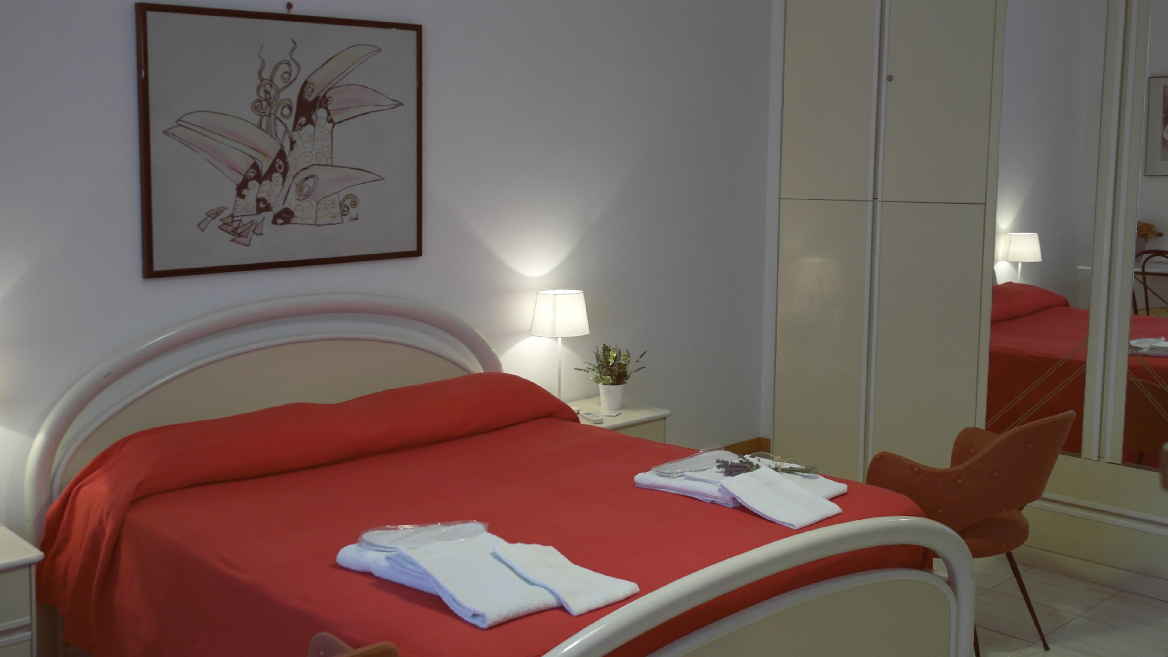 Una habitación de hotel con una cama, una mesita de noche, una lámpara, un espejo y una silla.