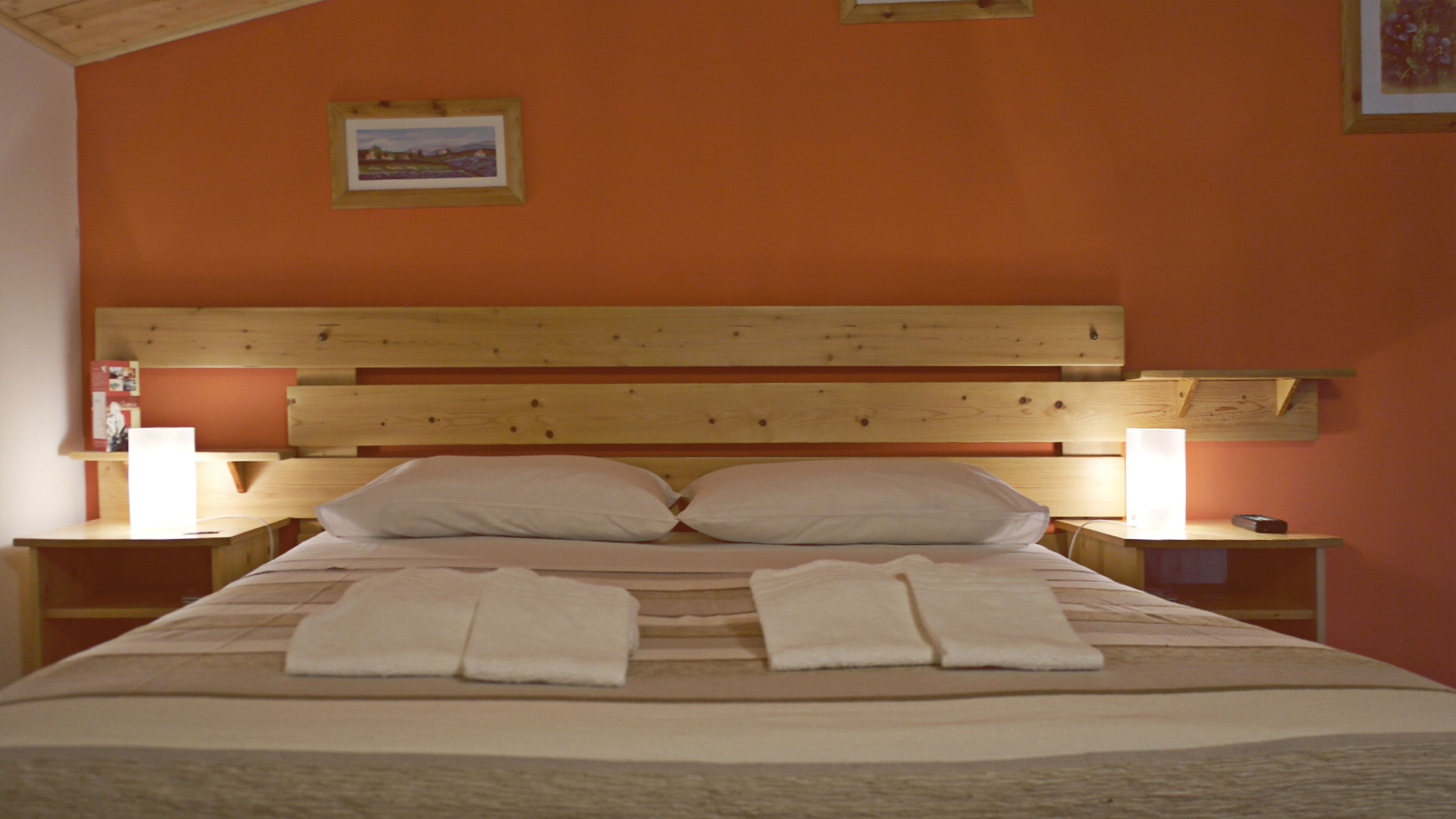 Un letto rifatto con due cuscini e due asciugamani piegati, una testiera in legno, due comodini con lampade e un quadro incorniciato al muro.