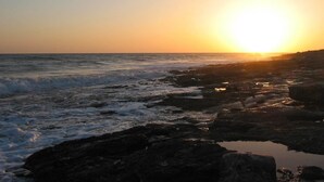 A sunset over a rocky coastline with waves crashing against the shore. - Giogaia Bed & Breakfast (Modica)