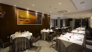 Un espace repas avec des tables dressées pour le service, un grand tableau accroché au mur et un design moderne au plafond.