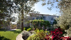 A stone building with a garden in front, featuring a variety of plants and a well-maintained lawn. - Tenuta Cammarana (Ragusa)