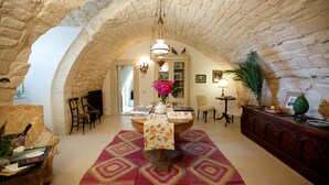 A spacious room with a high arched stone ceiling, a central table with a floral tablecloth, and a variety of seating options including a sofa and chairs. - Tenuta Cammarana (Ragusa)