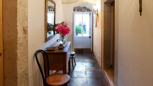 A hallway with a stone ceiling, a wooden bench, a chair, a vase with flowers, and a mirror on the wall. - Tenuta Cammarana (Ragusa)