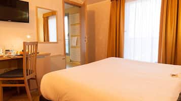 A hotel room with a large bed, a desk with a chair, a television, and a window with curtains.