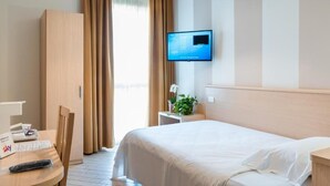 A hotel room with a bed, a desk with a chair, a television on the wall, and a window with curtains. - Hotel Mirandola (Mirandola)
