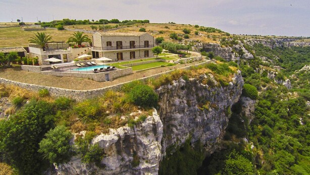 Una villa en el acantilado con piscina, mobiliario exterior y vistas del paisaje circundante.
