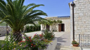 Un edificio de piedra con un patio empedrado, una palmera y flores coloridas.