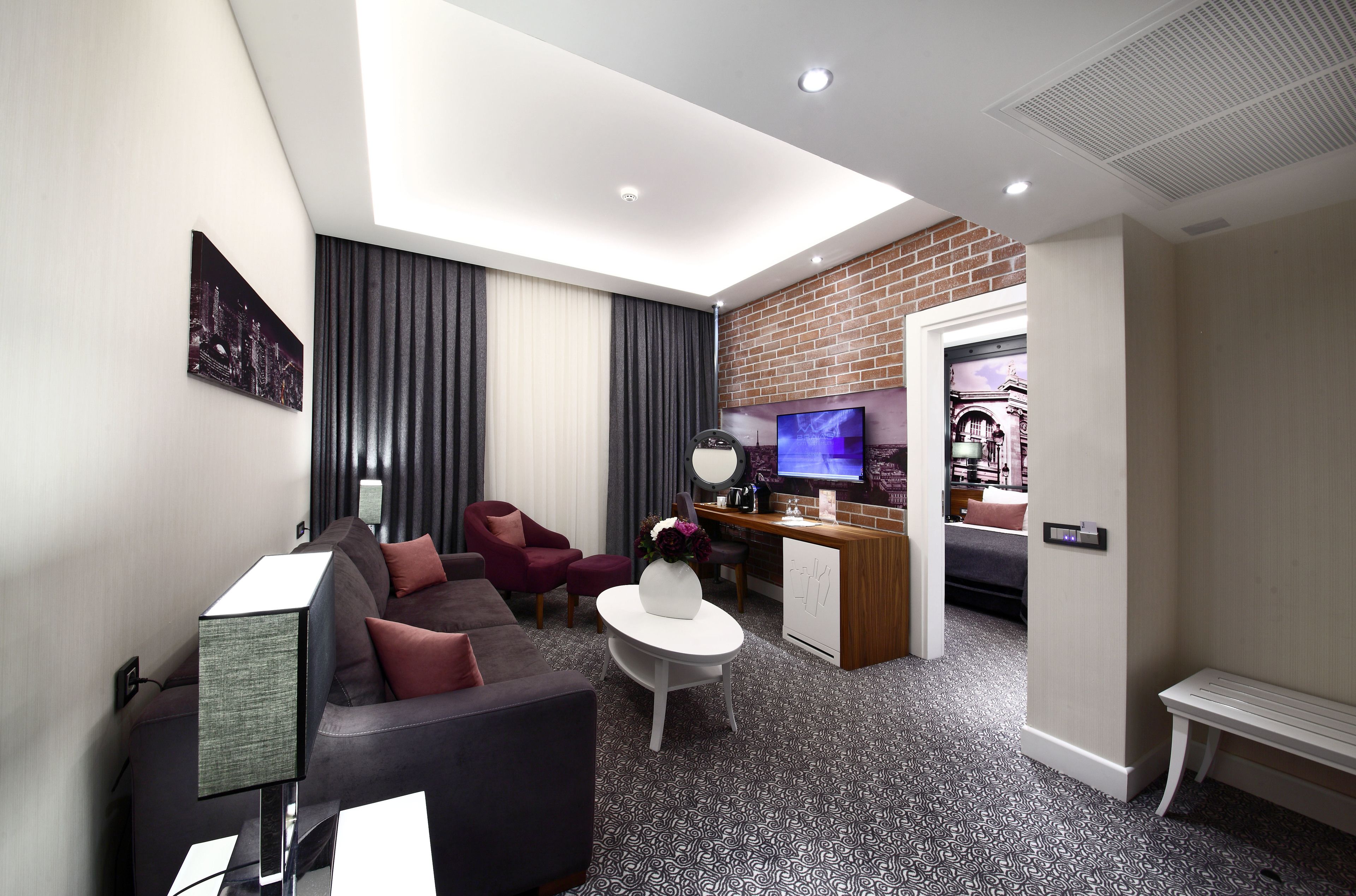 A modern hotel room with a living area, a dining area, and a TV.