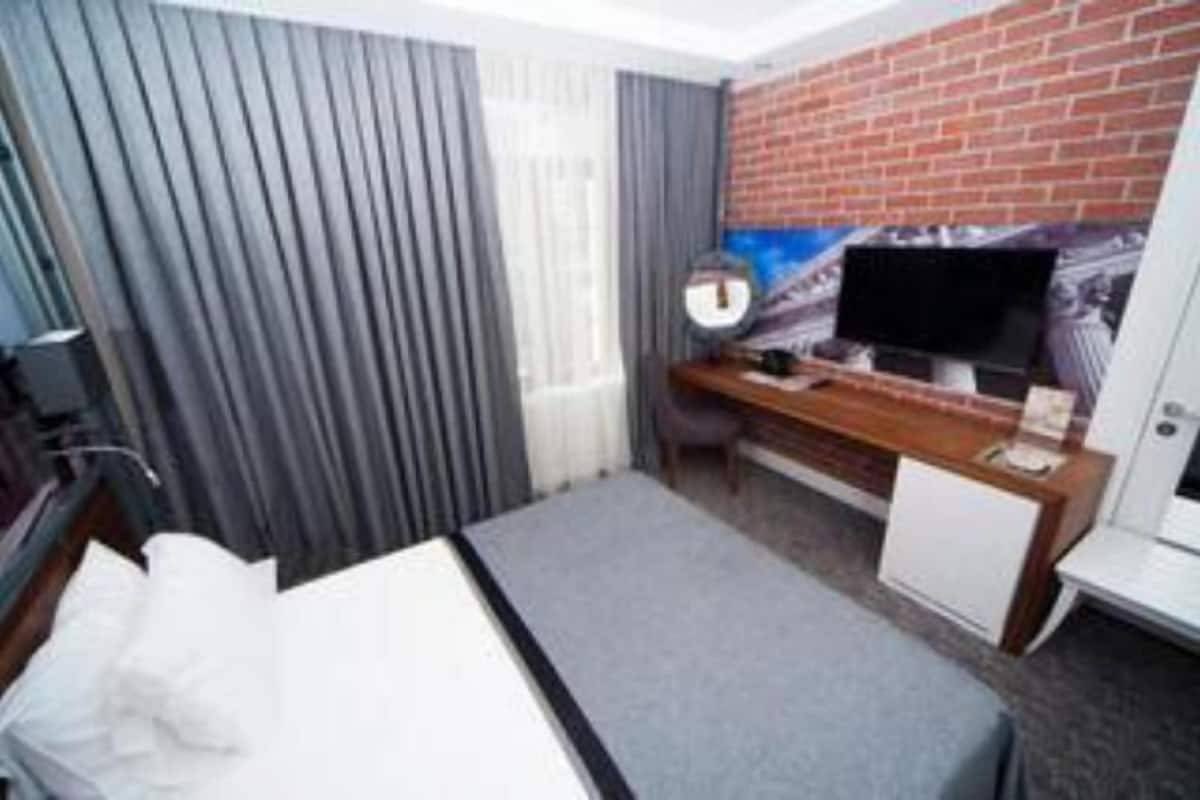 Habitació d'hotel amb un llit, un escriptori amb un ordinador, una televisió i una paret de maó.