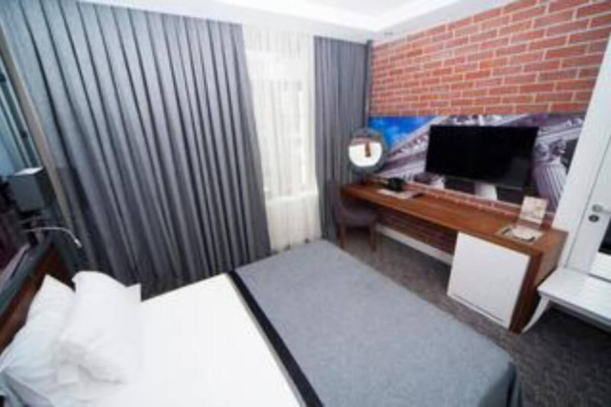 Habitació d'hotel amb un llit, un escriptori amb un ordinador, una televisió i una paret de maó.