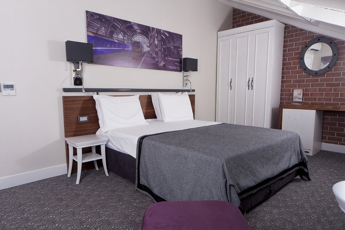 A hotel room with a bed, a small table, a chair, a wardrobe, a television, and a mirror.