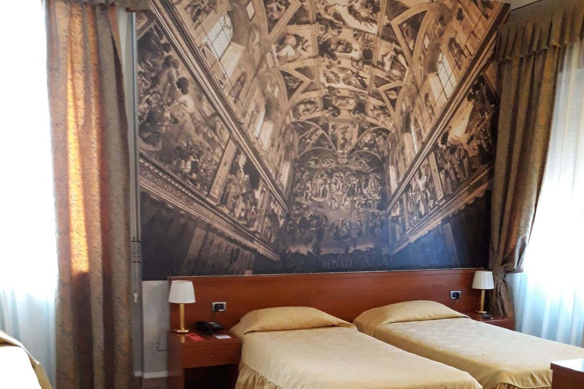 Habitación de hotel con dos camas, un mural grande en la pared y suelo de madera.