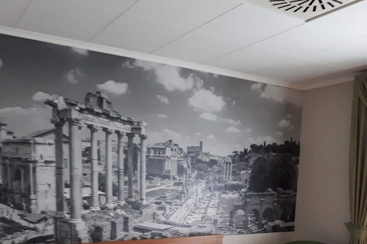 Una habitación de hotel con una cama grande, un sillón verde y un mural en la pared de ruinas antiguas.