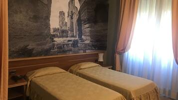 Ein Hotelzimmer mit zwei Betten, einer großen Wandmalerei antiker Ruinen, einem hölzernen Kopfteil und einem Fenster mit Vorhängen.