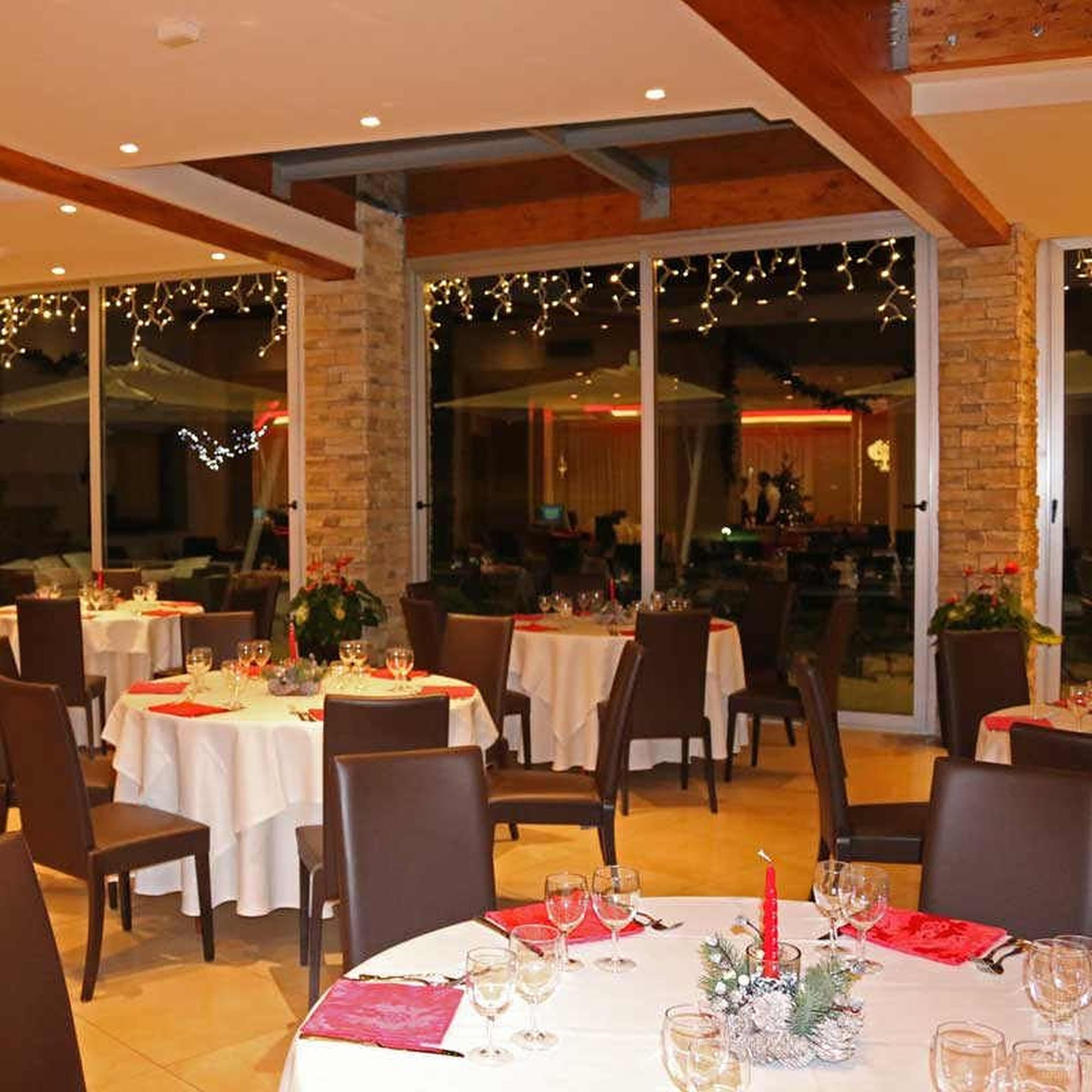 Een restaurant met ronde tafels gedekt voor een diner, met witte tafelkleden en rode servetten.