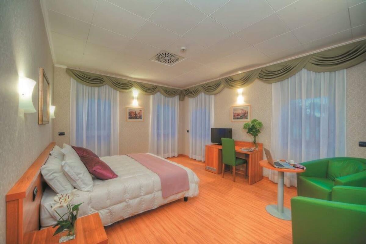 Habitación de hotel con cama, escritorio, silla y una mesita con una computadora portátil.