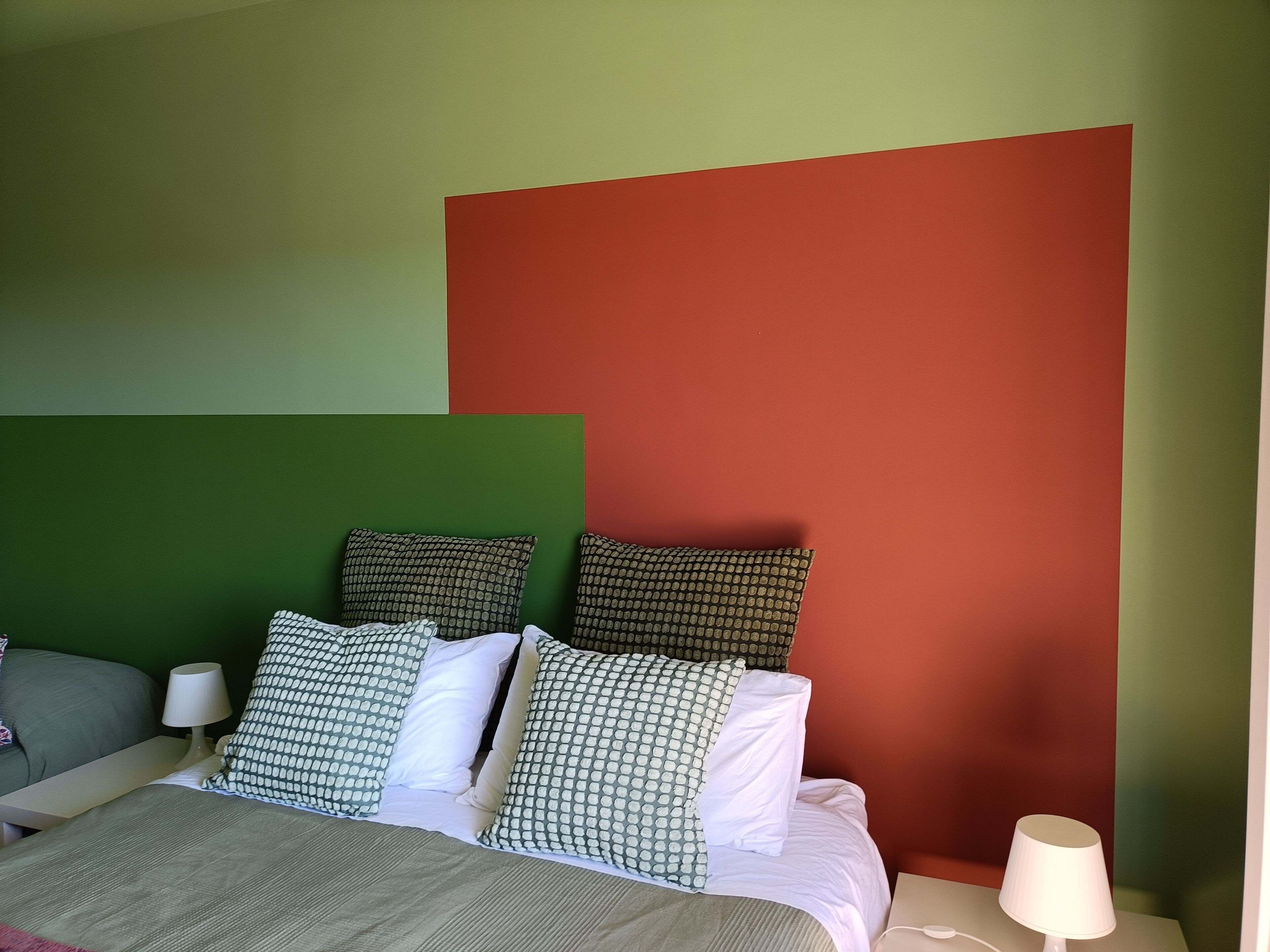 A bed with patterned pillows, a bedside table with a lamp, and a green and red wall.