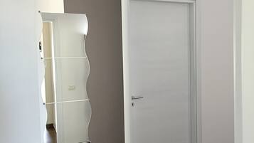 Ein Zimmer mit einer weißen Tür, einem Spiegel mit gewelltem Rahmen und einem Holzboden.